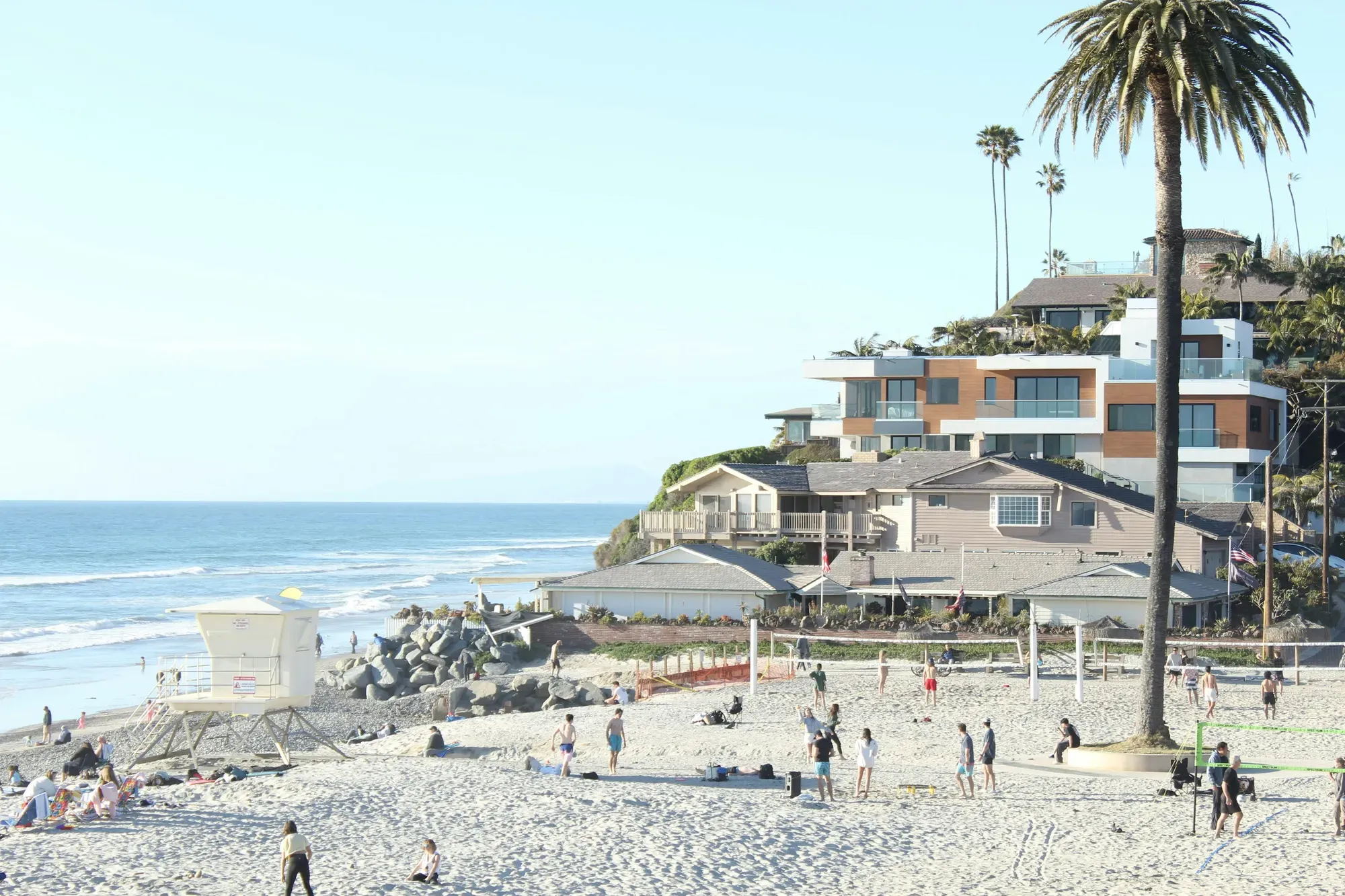 Beach houses perched on the bluff above a wide Encinitas beach, volleyball nets and a lifeguard tower on the sand below