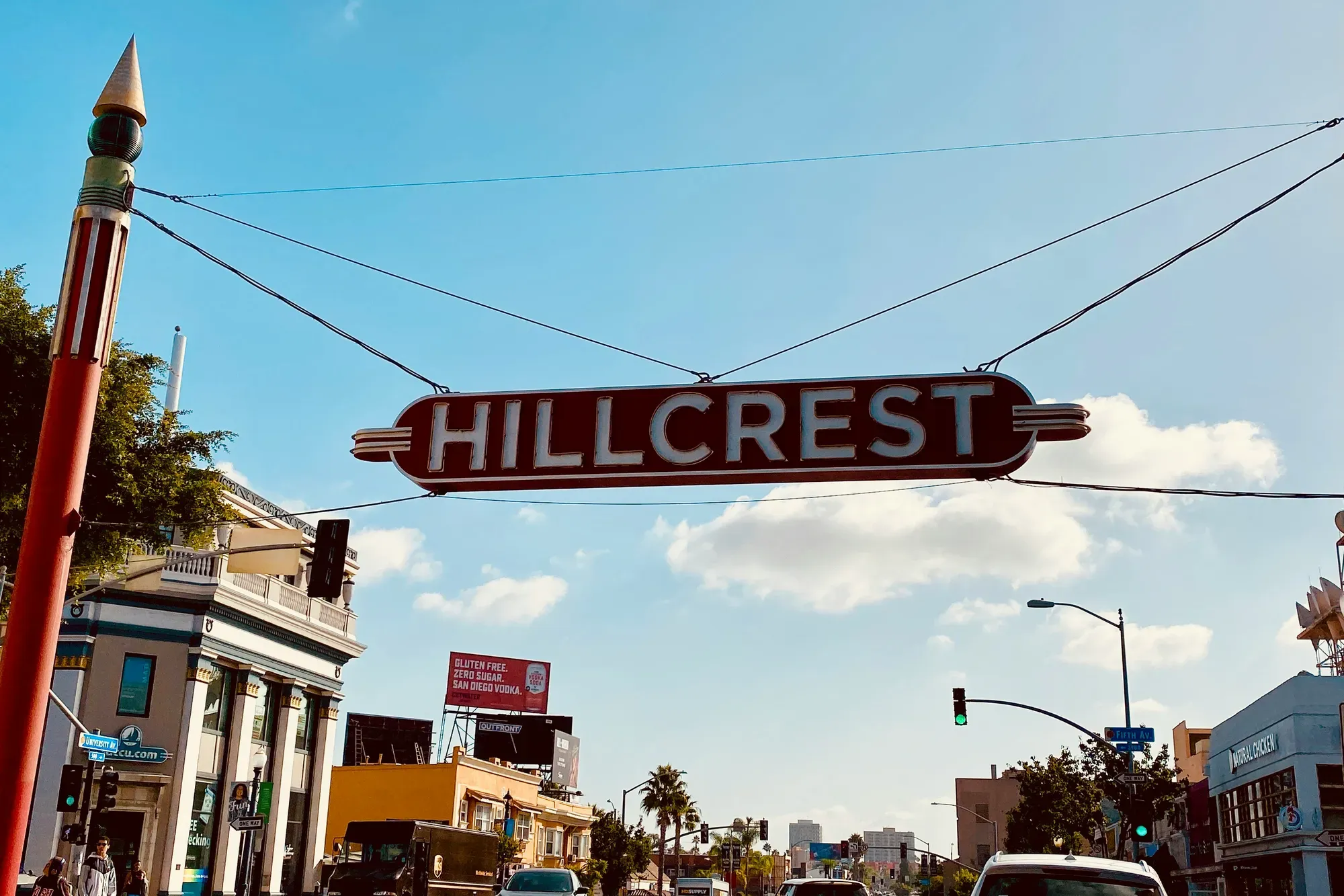 The red neon Hillcrest sign spanning University Avenue at Normal Street against a clear sky