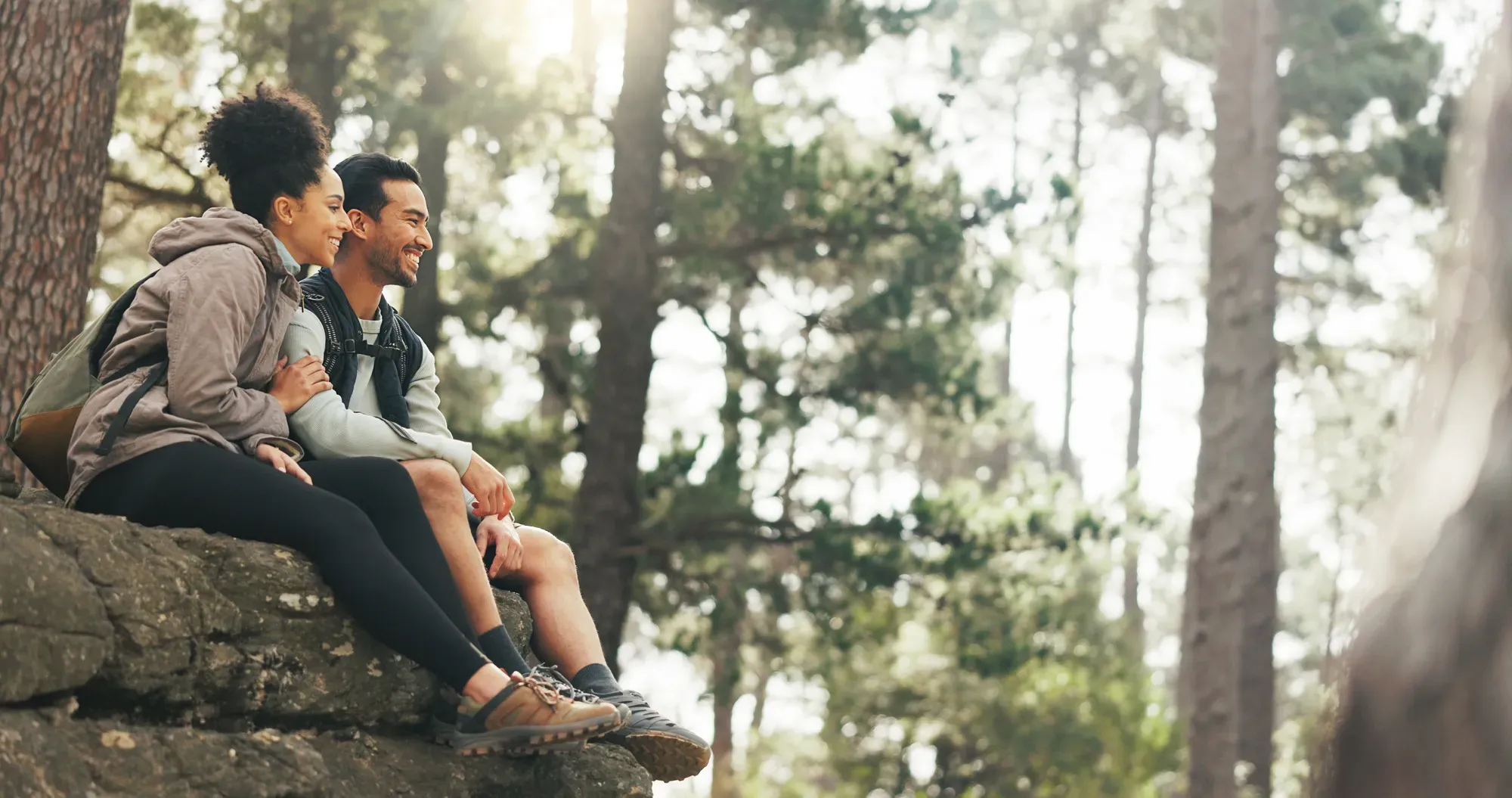 Two people sitting on a rock in a pine forest, laughing