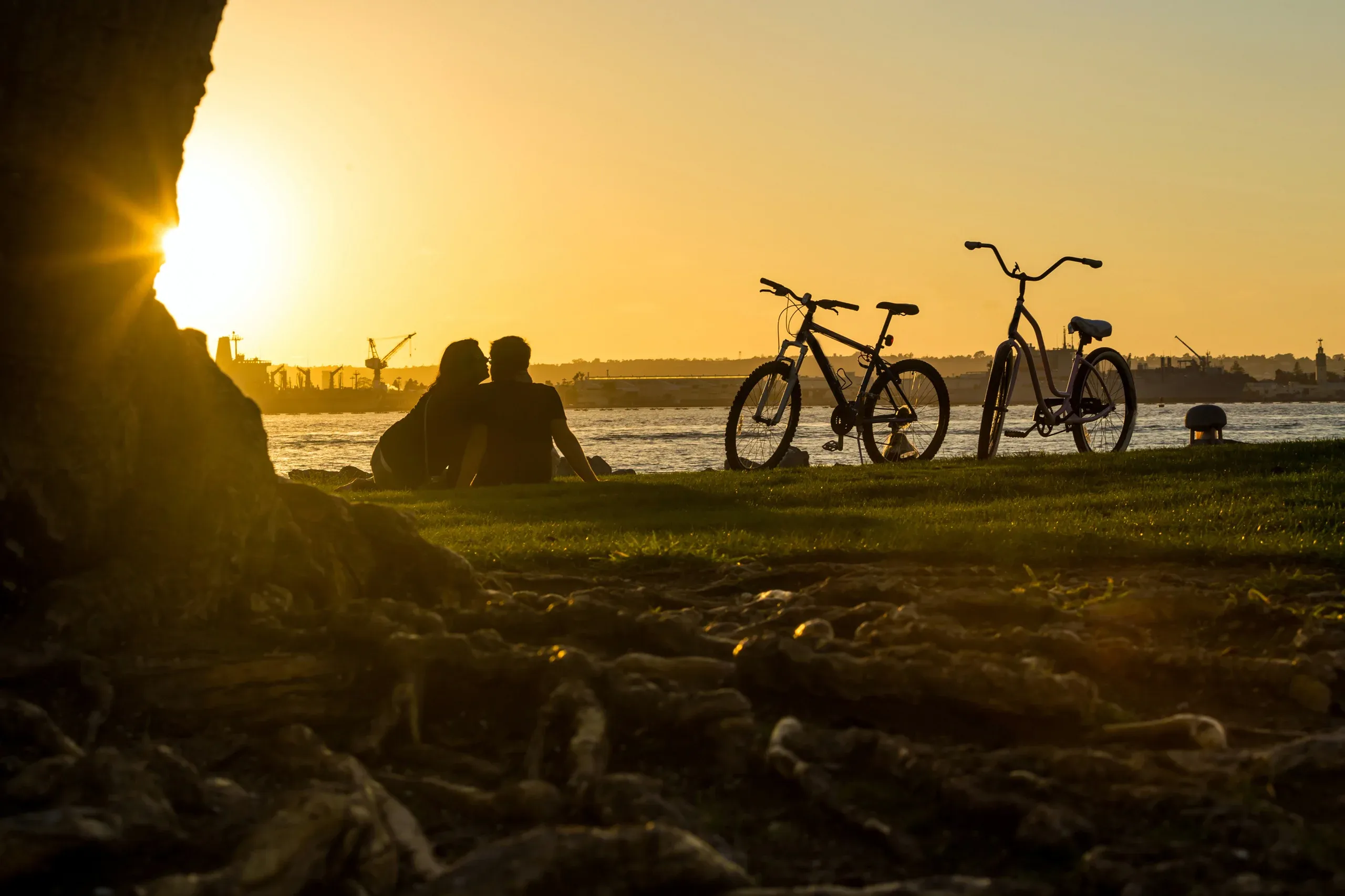 Two people sitting on the grass by San Diego Bay at sunset