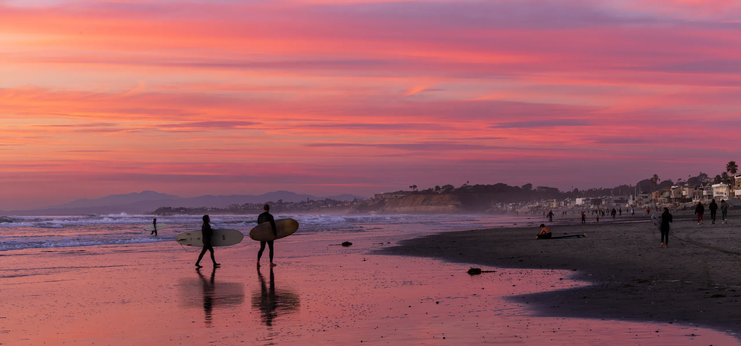 Two surfers carrying longboards across wet sand at sunset